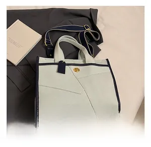 Detail of canvas tote with navy trim, gold twist lock, and wide striped shoulder strap