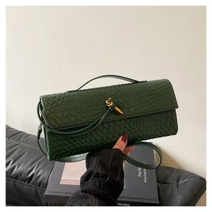 Detail of forest green woven baguette bag featuring a gold knot clasp and textured leather