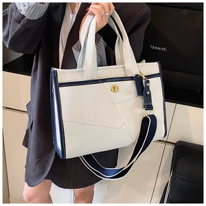 Detail of canvas and navy leather tote bag featuring a gold metal twist lock and wide strap