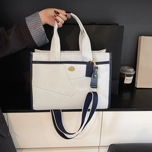Close-up of color-block canvas tote bag with metal turn-lock and wide fabric strap