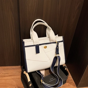 Detail of color-block tote bag with metal twist lock and decorative luggage tag