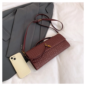 Detail of burgundy woven crossbody bag featuring elegant gold knot buckle and leather strap