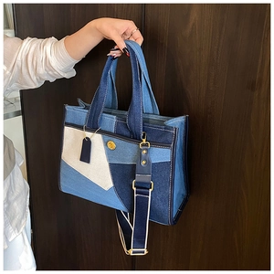 Detail of multi-color denim tote bag featuring wide striped strap and gold logo hardware