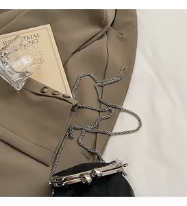 Detail of vintage black leather kiss-lock bag with silver chain on khaki blazer