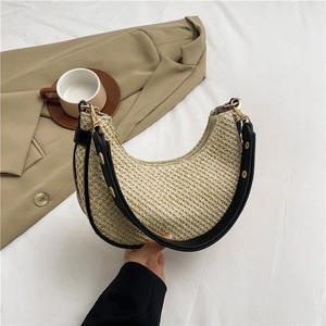 Striped straw hobo bag with black leather trim and gold studs held in a lifestyle setting