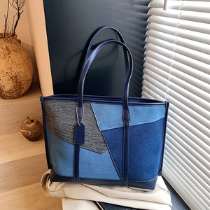 Gros plan détaillé d'un sac cabas en jean patchwork bleu avec anses en cuir sur un support