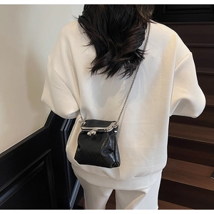 Detail view of black pleated mini bag with silver chain strap and metal clasp closure