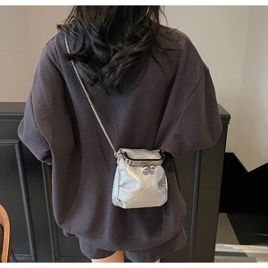 Detail of silver kiss-lock crossbody bag with pleated texture and metallic chain strap