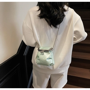 Model view of a mint green pleated crossbody bag with silver chain strap on a staircase