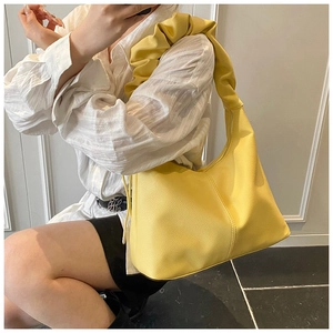 Detail of bright yellow leather shoulder bag featuring a unique gathered ruched strap design