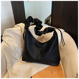 Detail of black pebbled leather tote with ruched handle and side drawstring on a chair