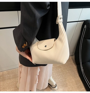 Detail of cream pleated shoulder bag with accordion texture and flap closure design