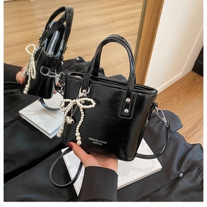 Détail du sac cabas en cuir verni noir avec pendentif nœud en perles et logo lettrage