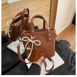 Détail d'un sac seau marron avec charm nœud en perles et pendentif cœur en métal