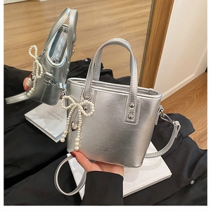 Détail du sac seau argenté avec texture cuir brillant et accessoire de nœud en perles