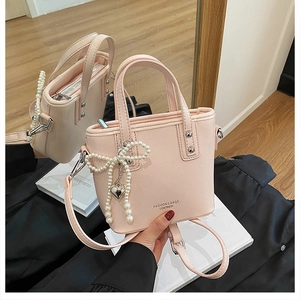 Mini sac seau rose en cuir avec pendentif nœud perlé et reflet sur une surface miroir