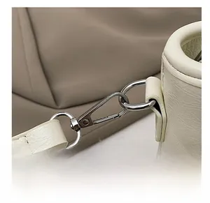 Gros plan du crochet en métal argenté et chaîne perlée sur un sac seau en cuir crème