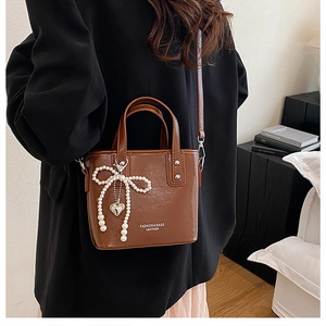 Détail du sac seau en cuir marron avec nœud en perles et breloque en forme de cœur
