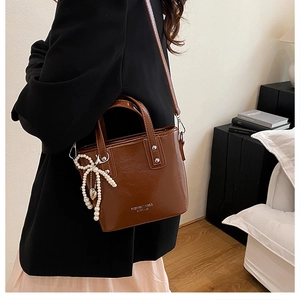 Sac seau en cuir marron avec nœud en perles et pendentif cœur porté par mannequin