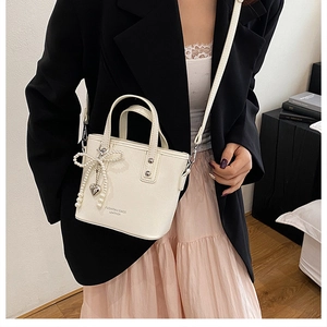 Détail du sac seau crème avec nœud en perles et breloque cœur porté par un mannequin