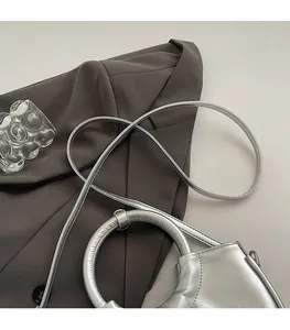 Detail of silver metallic saddle bag with unique circular handle and slim shoulder strap
