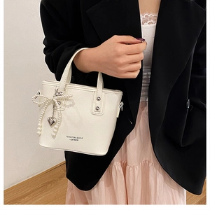 Détail du sac seau en cuir blanc avec texte fashion et breloque perle et cœur