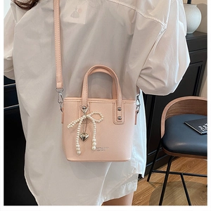 Détail d'un sac seau rose avec nœud perlé et breloque cœur porté par un mannequin