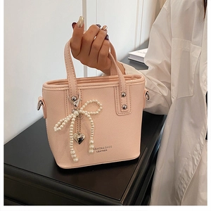 Détail du sac seau rose avec nœud en perles et pendentif cœur sur texture en cuir