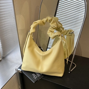 Minimalist light yellow leather shoulder bag with ruched handle shown in soft lighting