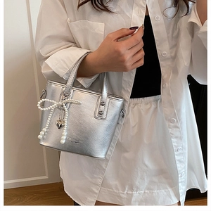 Détail du sac seau argenté avec logo embossé et breloque nœud en perles