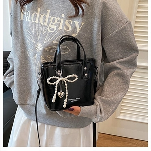 Détail du sac seau en cuir noir brillant avec nœud en perles et pendentif coeur