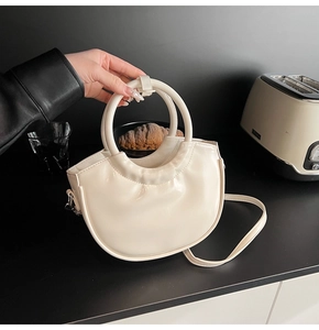 Detail of cream patent leather crescent saddle bag with round handle and shiny finish