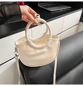 Detail of a creamy white crescent saddle bag showing smooth PU leather and round top handle