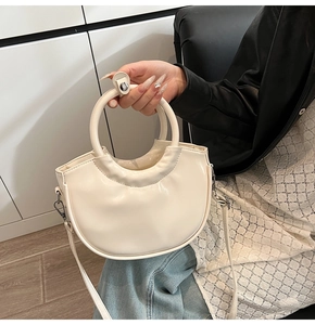Detail of cream white half-moon saddle bag with smooth leather finish and top handle