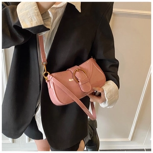 Détail du sac en cuir verni rose avec boucle fer à cheval dorée sur un blazer noir
