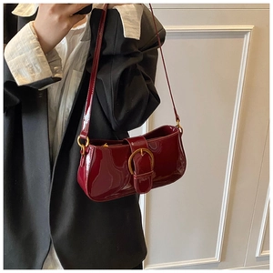 Détail du sac à main en cuir verni bordeaux avec boucle dorée porté par un mannequin