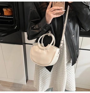 Detailed view of a creamy white half-moon saddle bag with round handle and shoulder strap