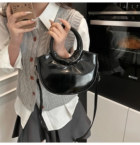 Close-up of black glossy saddle bag with round handle and adjustable strap worn by model