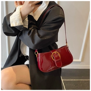 Détail d'un sac baguette en cuir verni bordeaux avec une boucle en fer à cheval dorée