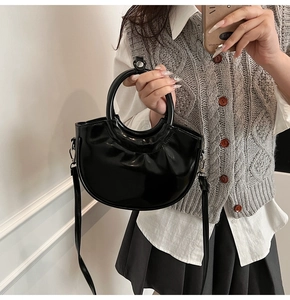 Detail of black glossy leather saddle bag featuring a circular handle and silver hardware
