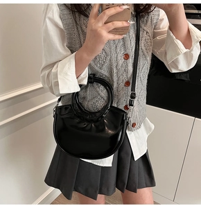 Black half-moon saddle bag with round handle and leather strap shown in a mirror selfie