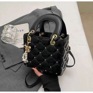 Détail d'un sac à main noir matelassé avec clous étoiles dorés et perle