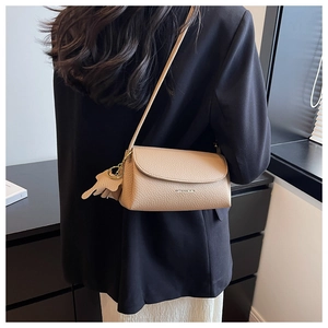 Close-up of beige litchi grain leather crossbody bag with tassel detail on model