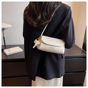 Detail of cream pebbled leather shoulder bag with a cute elephant charm on a model
