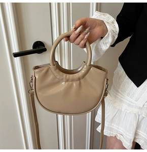 Close-up of stylish light brown saddle bag with circular handle held against a door