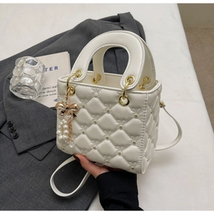 Gros plan détaillé d'un mini sac à main blanc matelassé avec nœud doré et perle