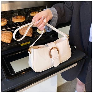 Détail du sac en cuir verni blanc cassé avec boucle bronze dans une ambiance de boulangerie