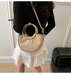 Detail of a chic beige moon bag with a unique circular handle and smooth faux leather finish