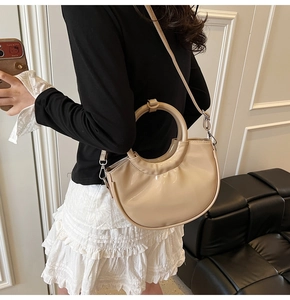 Detail of beige glossy saddle bag with unique round handle and detachable shoulder strap