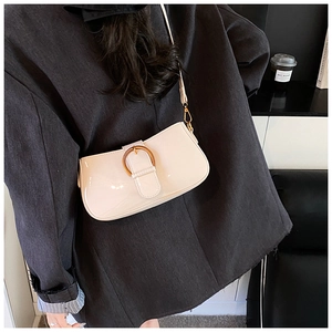 Détail d'un sac sous le bras crème brillant avec boucle ronde porté avec un manteau noir